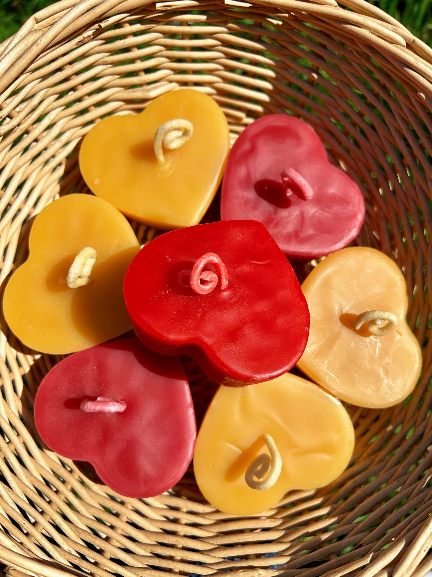 Heart-shaped beeswax candles in red, pinkand yellow on a wicker basket
