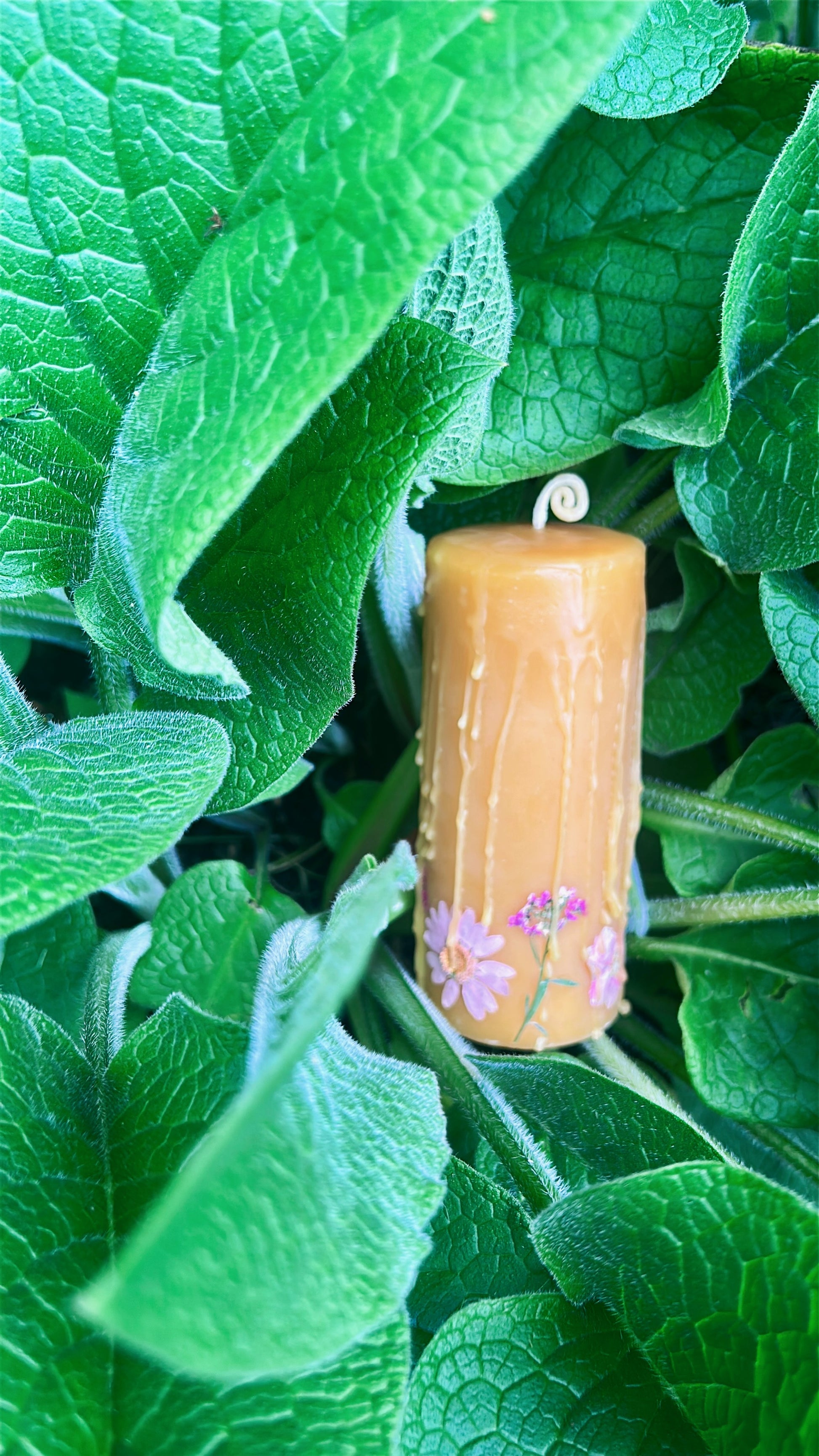 Beeswax candle with floral design on green leaves