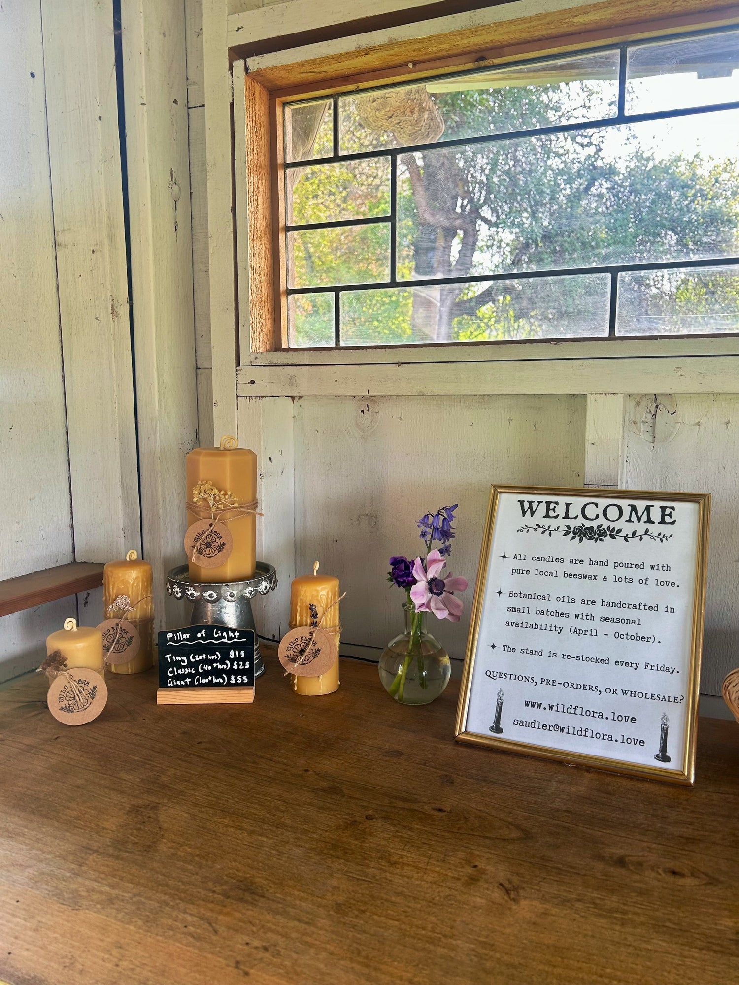 Decorative setup with beeswac candles, a vase of flowers, and a 'Welcome' sign on a wooden surface.