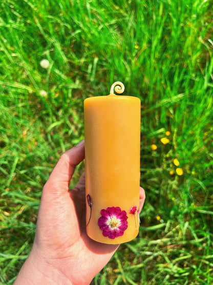 Hand holding a beeswax pillar candle with pink flower design against a grassy background