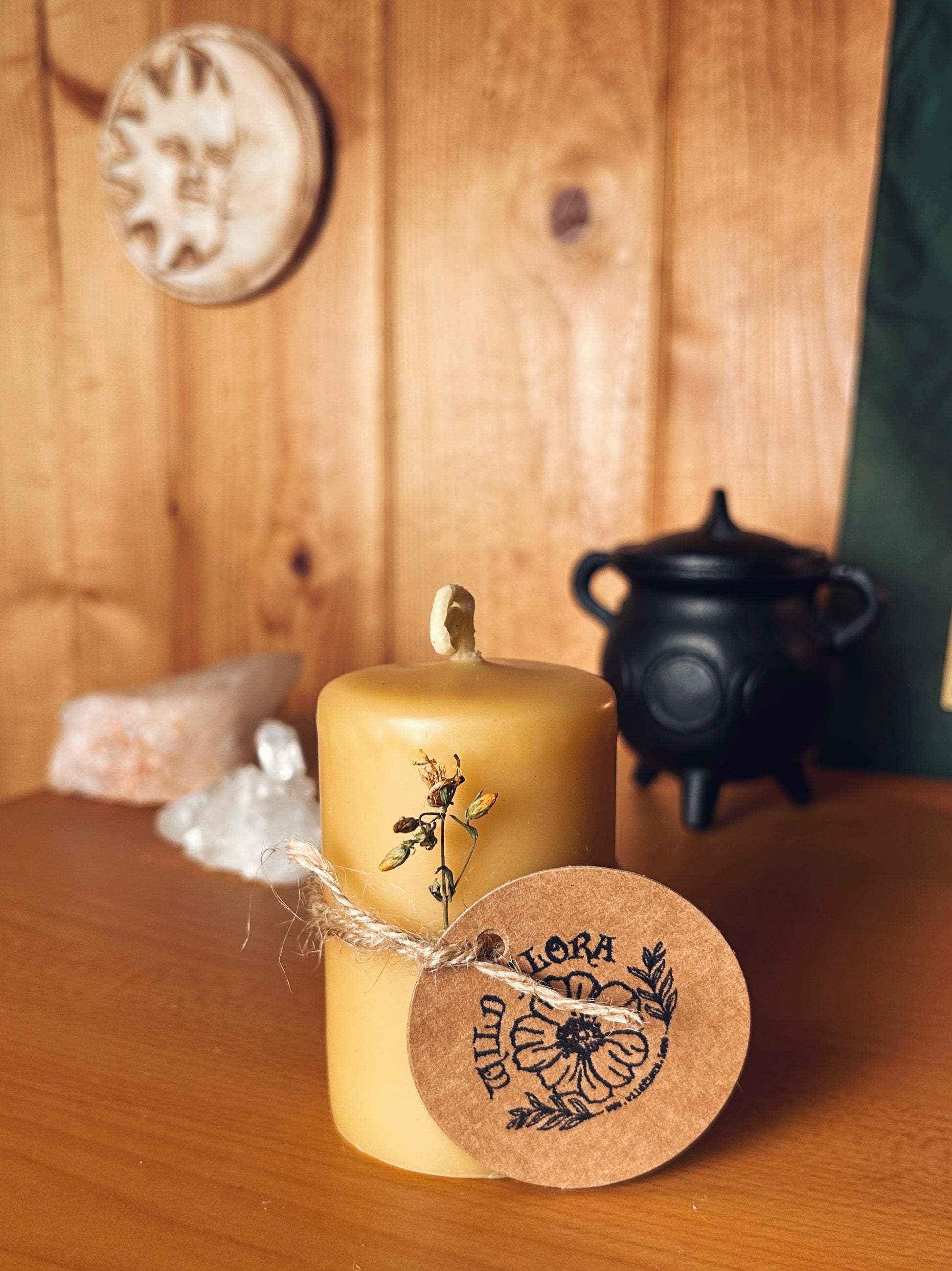 Beeswax pillar candle decorated with st john's wort and twine. Cauldron, clear caurtz and rose quartz in background. Whimsical squiggly wick.