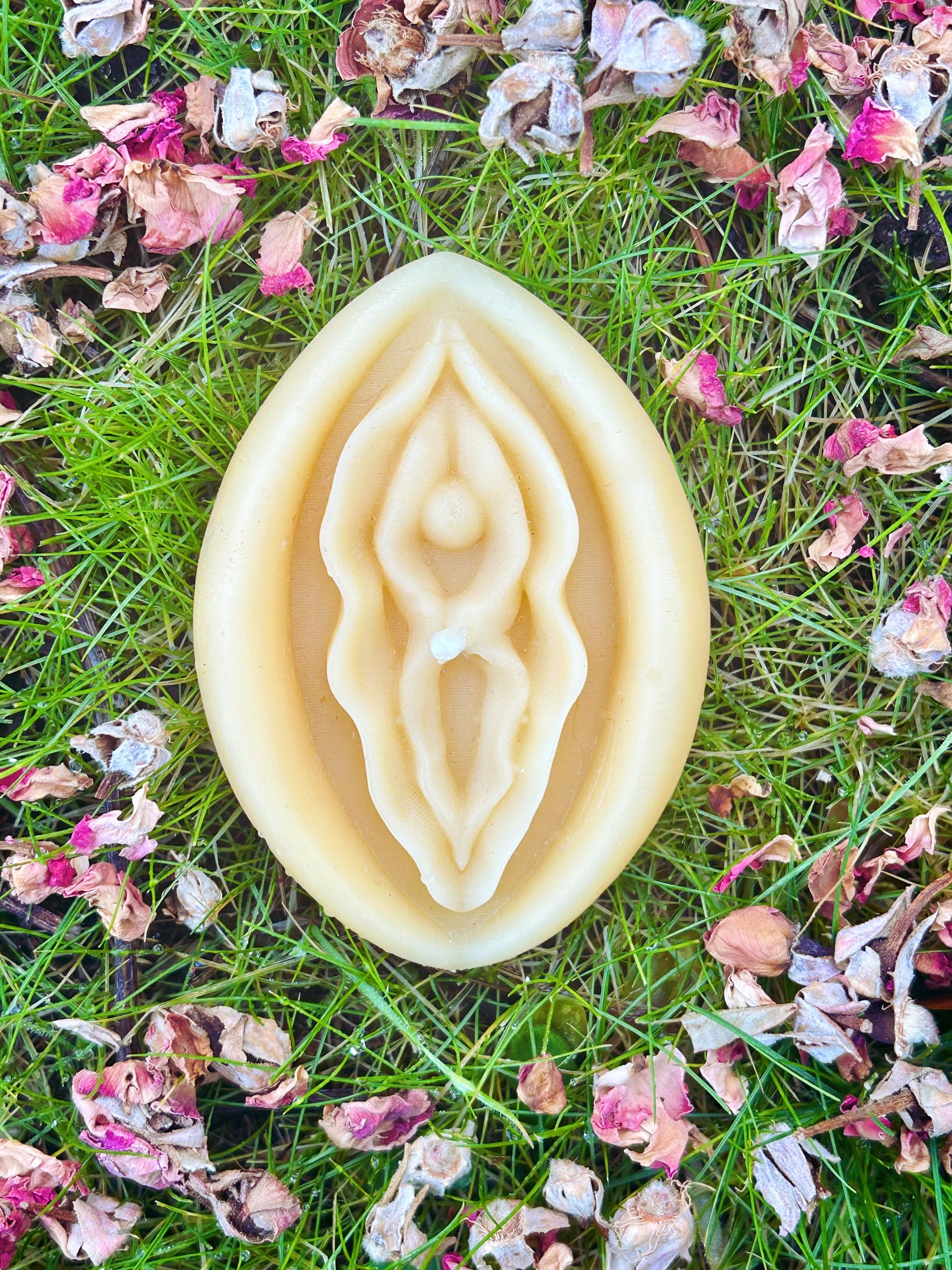 Beeswac vagina candle on grass with rose petals.
